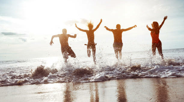 Four happy friends having fun and runs to sunset sea beach.